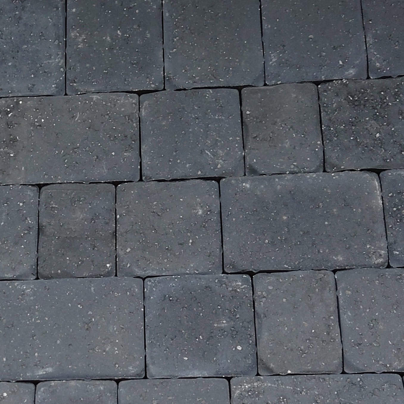 A close-up of a paved stone surface displays Cemex 50mm ReadyPave CAMDEN Charcoal bricks in a staggered pattern, featuring rectangular, dark charcoal bricks with a textured, slightly rough surface.