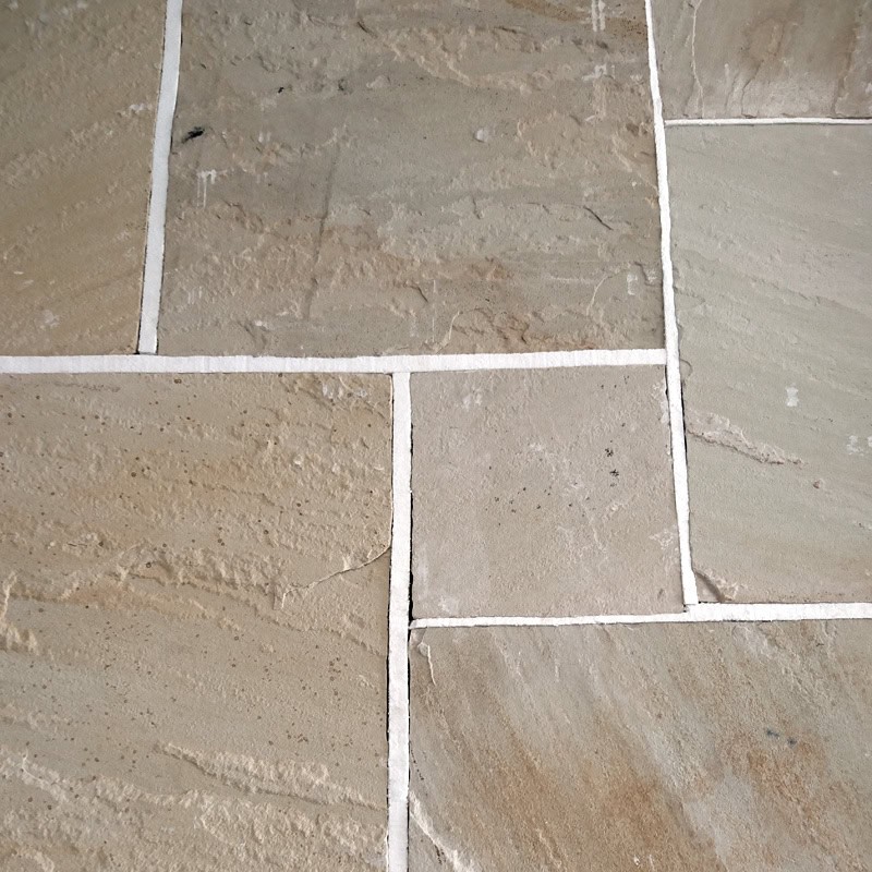 A close-up of the Strata 22mm Calibrated Sandstone MINT shows a beige tile floor with white grout between rectangular tiles, featuring a rough, textured surface in various shades and patterns for a natural and rustic look.