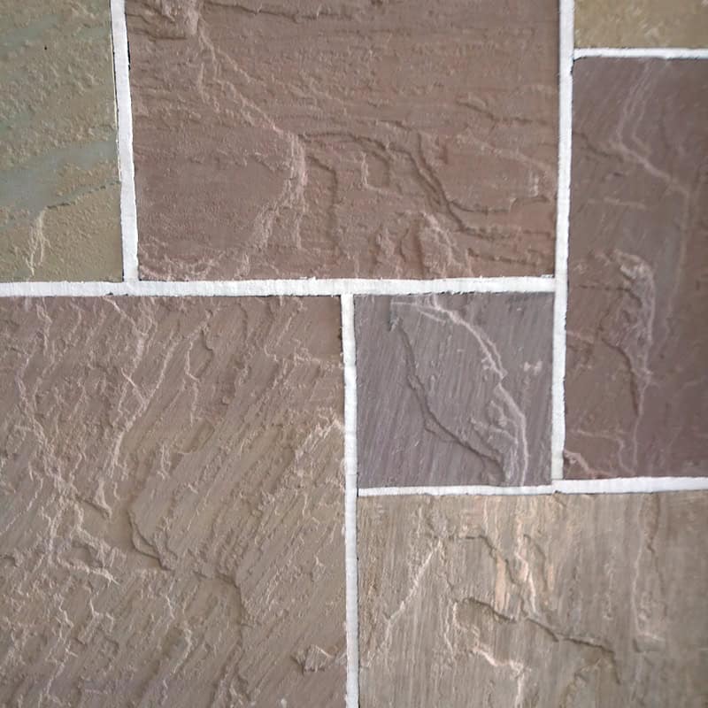 Close-up of a wall with Stone Pave 22mm Calibrated Sandstone GOLDEN BUFF Mix tiles, featuring brown, gray, and beige tones. The rough-textured stones are arranged in a staggered pattern with visible white grout lines and hints of golden buff.