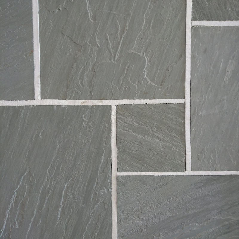 A close-up of Strata 22mm Calibrated Sandstone GREY tiles, displaying a greyish-green hue. The rectangular tiles are offset and separated by light-colored grout lines, showcasing a textured surface with fine natural striations.