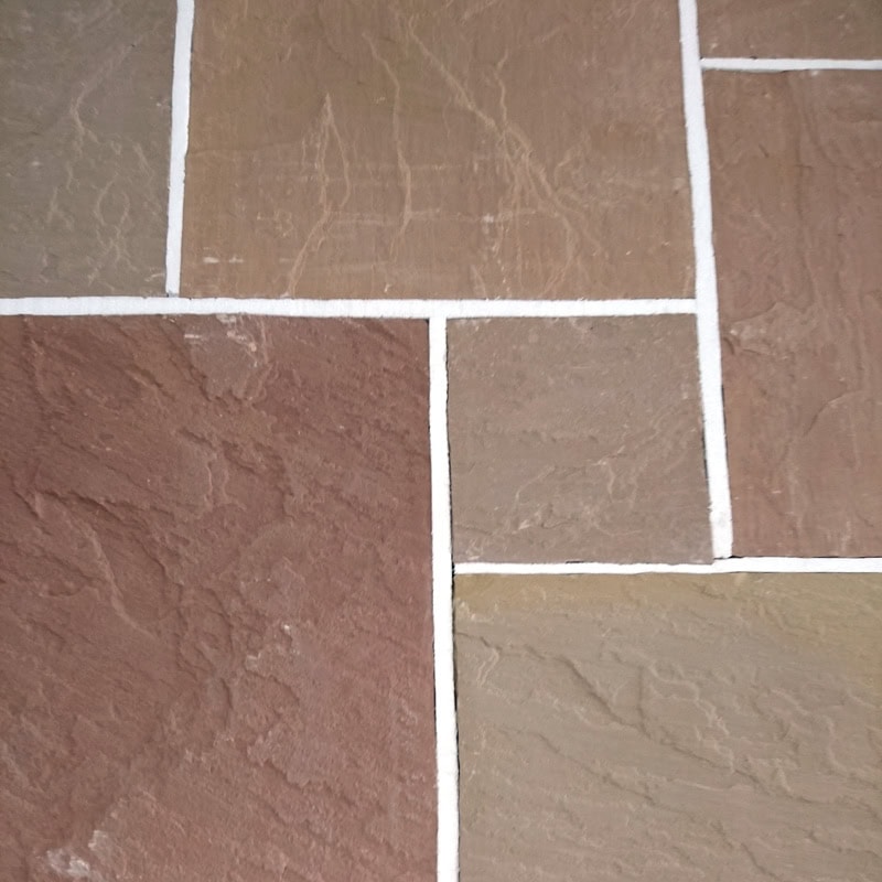 Close-up of a stone tile floor with a rectangular pattern featuring Strata 22mm Calibrated Sandstone MODAK. The tiles vary in shades of brown, gray, and beige, separated by white grout lines, highlighting the textured surface.