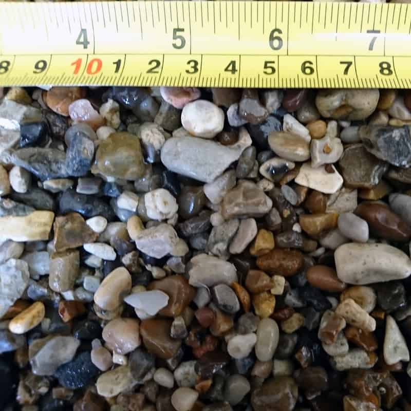 A close-up shows Natural Rounded 10mm Blue/Grey Pebbles with a yellow measuring tape above, marked in centimeters and inches, displaying measurements up to 10 cm and 4 inches.