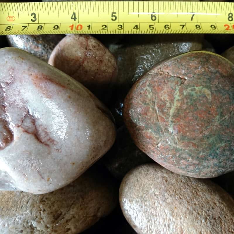 The Scottish Highland Pebbles 50-80mm - Bagged are displayed with a measuring tape showing a length of approximately 7.5 cm.