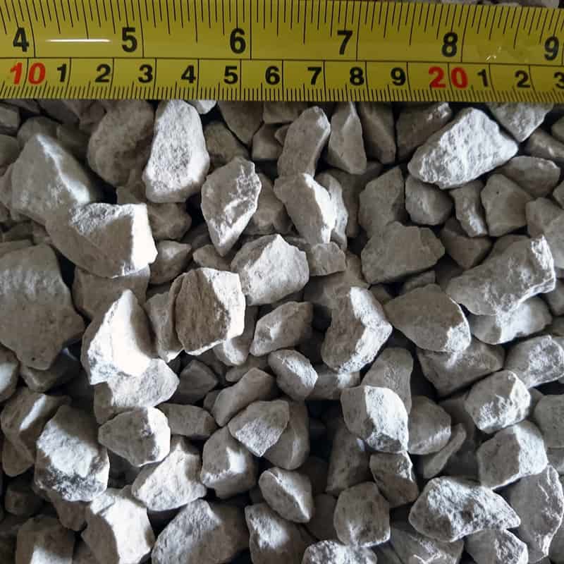 A pile of small, irregularly shaped Cotswold Buff 20mm chippings is shown with a yellow measuring tape on top, displaying sizes from 9 to 20 cm in length.