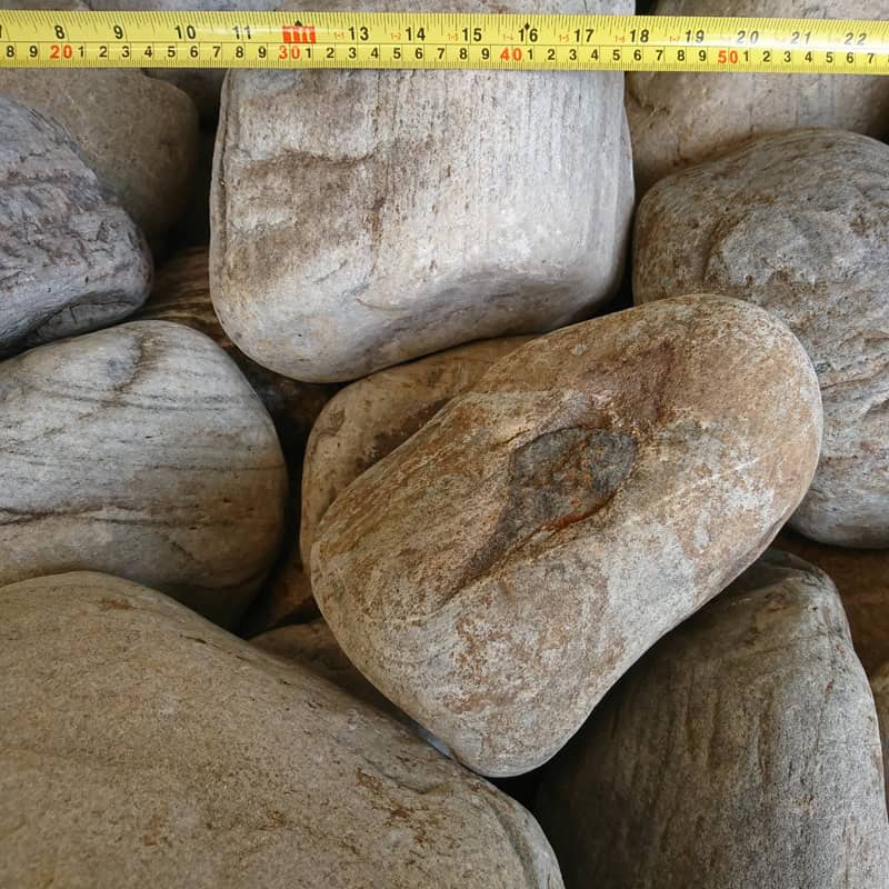 A close-up shows multiple 200-300mm Highland Glacial Cobbles stacked together, with a tape measure displaying centimeters up to 50. The cobbles display subtle lines and textures in shades from light to dark gray.