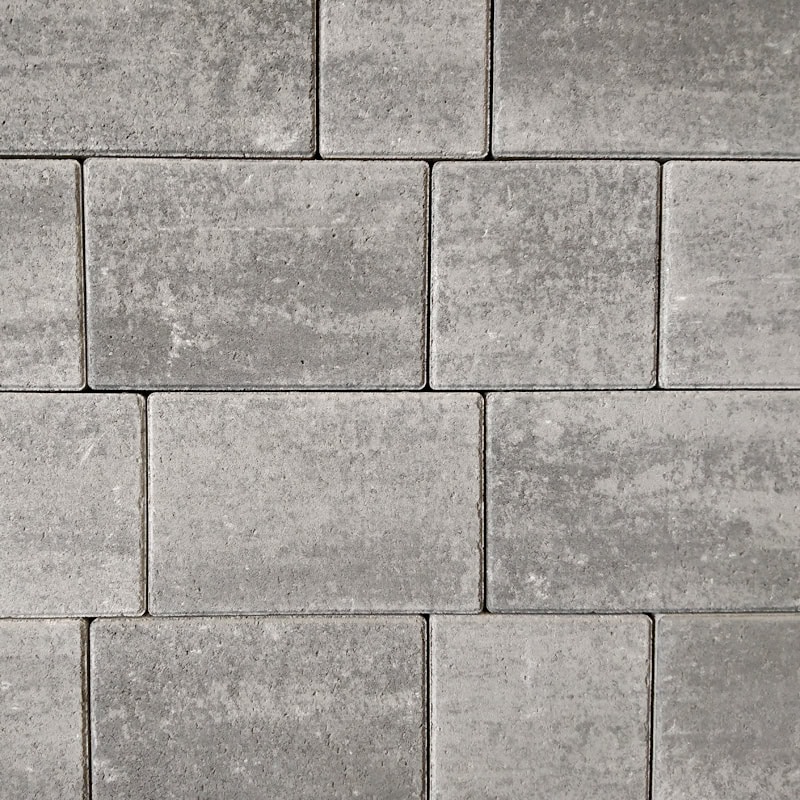 A staggered pattern of light gray Barleystone 60mm Castlepave Smooth Silver Grey bricks forms a seamless wall. The surface features a slightly rough feel with subtle shade variations, enhancing its rustic charm.