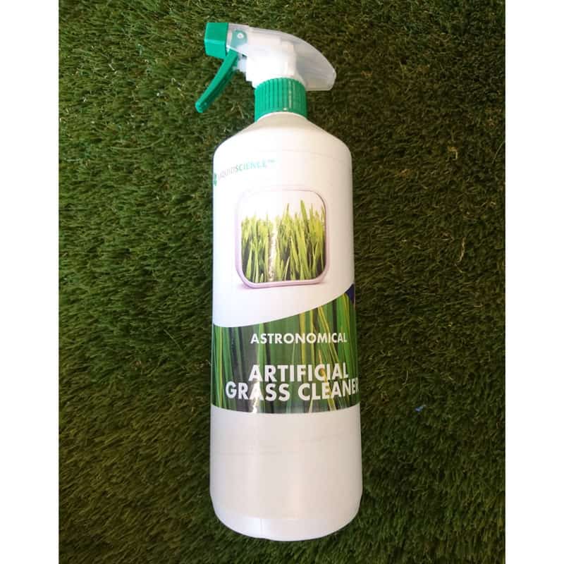 A bottle of Artificial Grass Cleaner with a spray nozzle rests on a verdant turf surface. The label displays lush grass blades, and the bottle is mostly white with green and black accents.