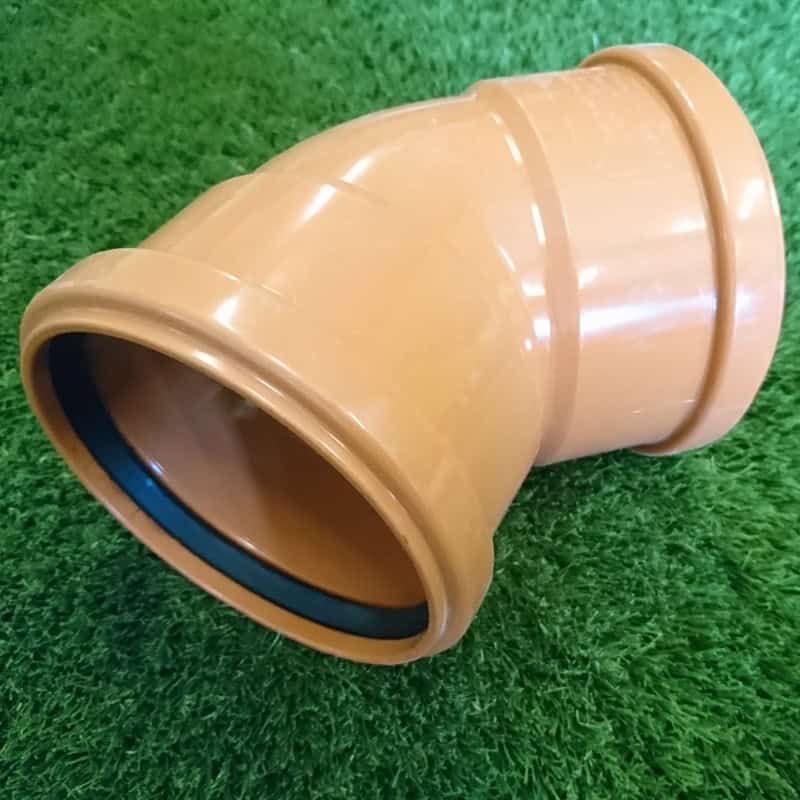 A 110mm 45° Double Socket Bend, brown plastic pipe elbow connector with a rubber seal, is nestled on green grass.