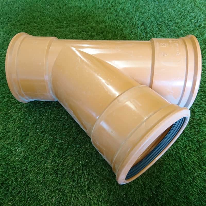 A 110mm tan plastic Y-shaped plumbing pipe connector with a 45° junction and triple socket design rests on green artificial grass.