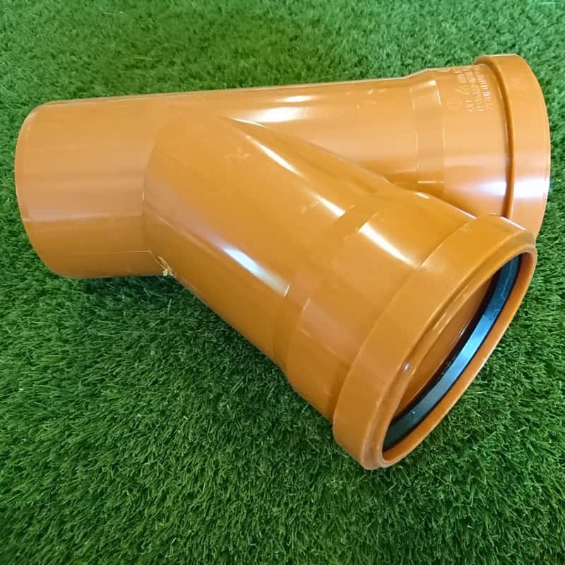 The 110mm 45° Double Socket Junction, an orange plastic Y-shaped pipe fitting for improved connectivity, is set on artificial green grass.