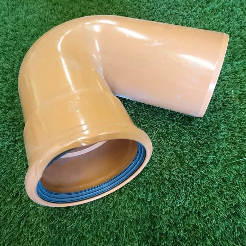 A brown PVC pipe elbow with a rubber seal for plumbing lies on grass, seamlessly fitting the 110mm Single Socket Gully Trap for efficient drainage.