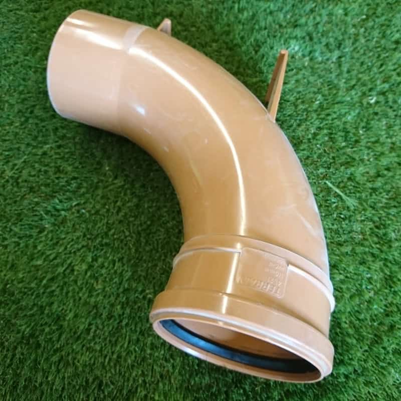 A 110mm Single Socket 90° Rest Bend plumbing pipe, brown and plastic with a rubber seal, is on a grass surface.