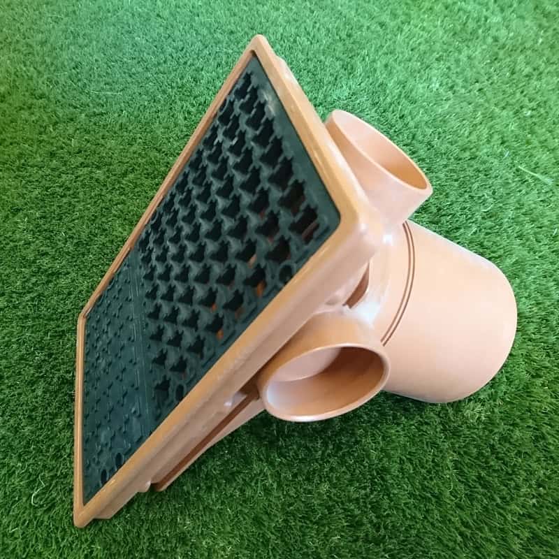 The 110mm Rectangle Hopper Spigot End, a brown plastic drainage fitting with a rectangular grid cover and circular openings, is angled on green grass for seamless integration into the landscape and efficient water flow management.