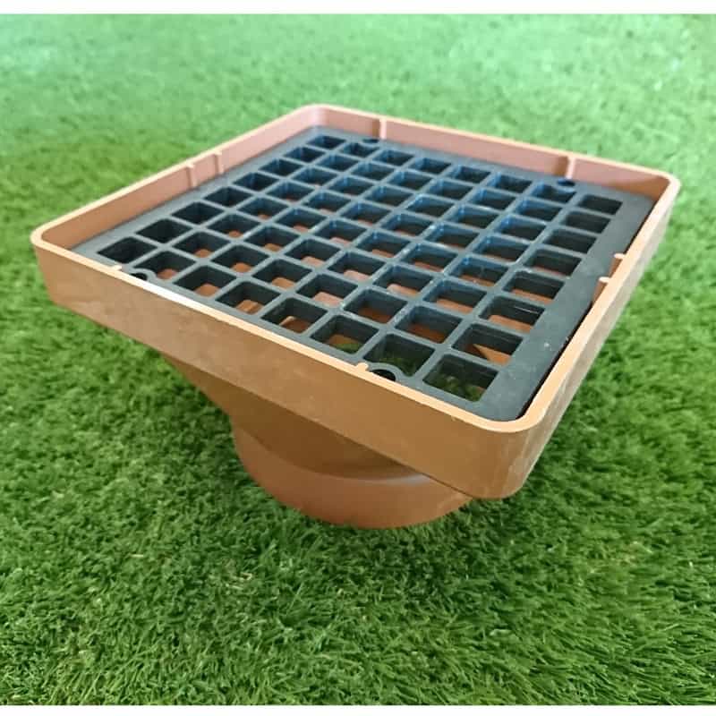 A 110mm Square Hopper Socket End with a sloped design and black grid cover rests on lush green grass, leading to a circular base compatible with 110mm socket end fittings for efficient drainage.