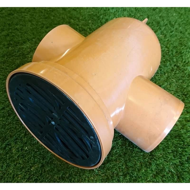 A brown plastic 110mm Round Back Inlet Bottle Gully with two side openings and a black grated top cover sits on the green grass.