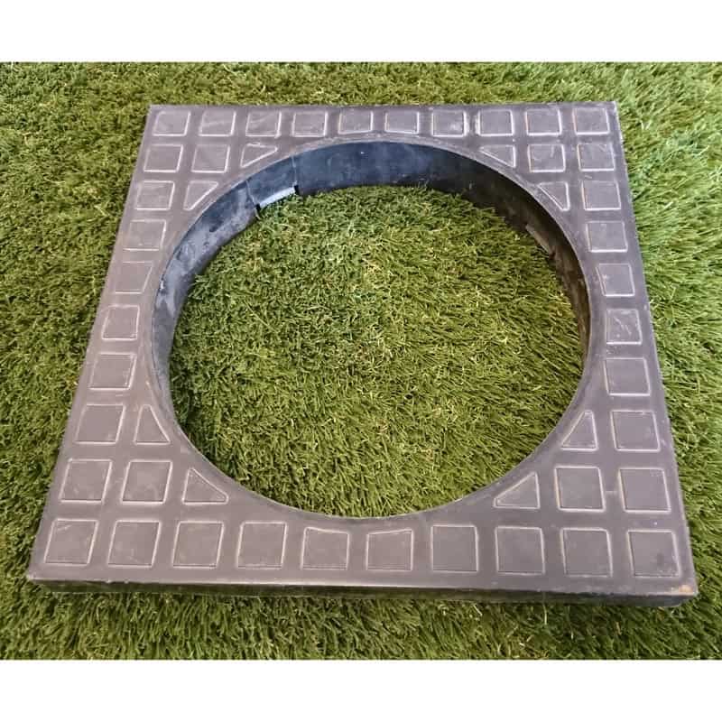 The 110mm Bottle Gully Square Adaptor, with a central circular opening for a 110mm bottle gully, rests on artificial grass. Its checkered pattern offers elegance and functionality.