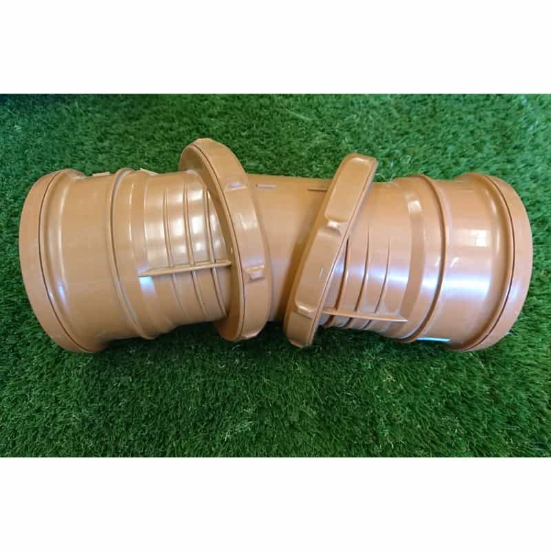 The 110mm Double Socket Adjustable Bend, a brown plastic drainage pipe connector with a ribbed design, is displayed on green artificial grass.