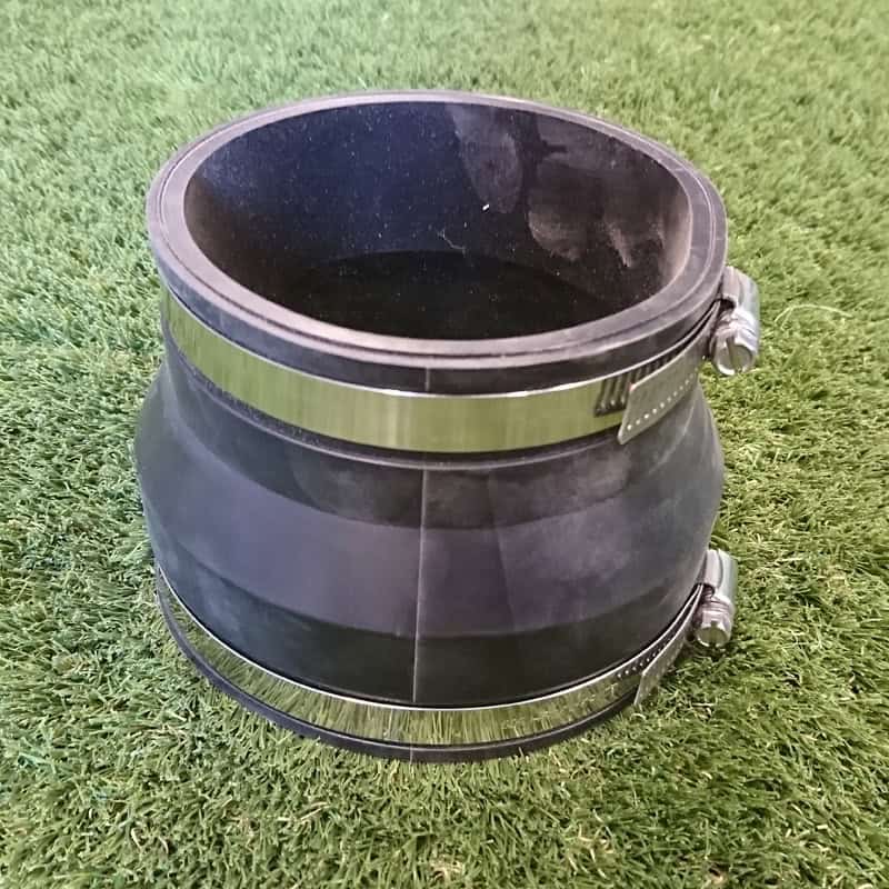 A 110mm Clay to UPVC Coupling, a black rubber cylinder with adjustable metal clamps on each end, rests on green grass.