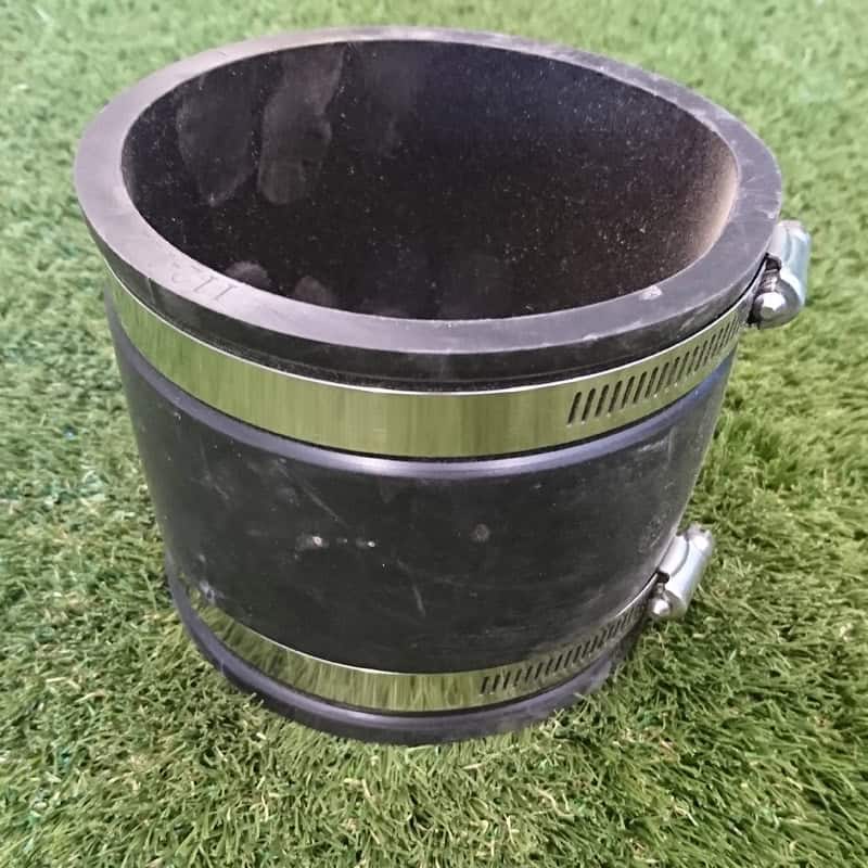 The 110mm Flexible UPVC Coupling, featuring a black rubber finish and metallic clamps on both ends, elegantly rests on a grassy surface, turning a basic 110mm connection into an adaptable marvel.