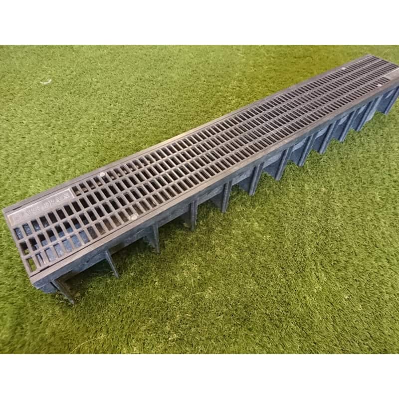 The Clark Deep Drain Unit is a long black plastic drainage channel with evenly spaced rectangular openings, placed on grassy surfaces for efficient outdoor water drainage and optimal flow management.