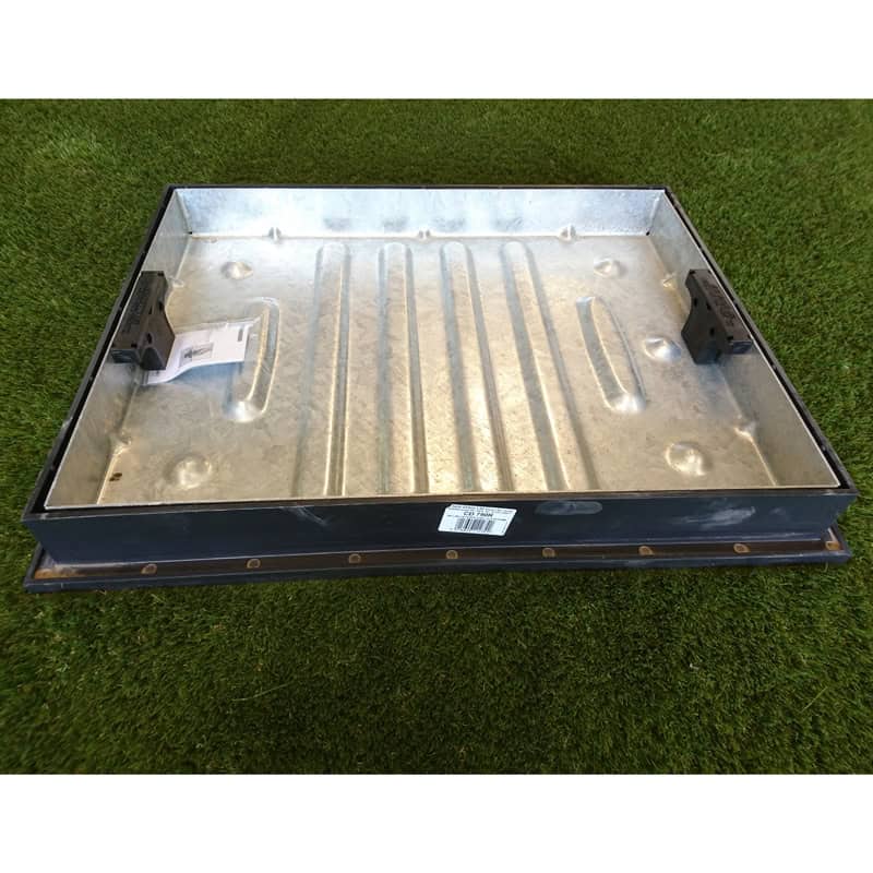 A 600x450x46mm metal Recess Cover & Frame with a rectangular shape, raised edges, grooves on the bottom, black brackets inside, and a white label is set on grass.