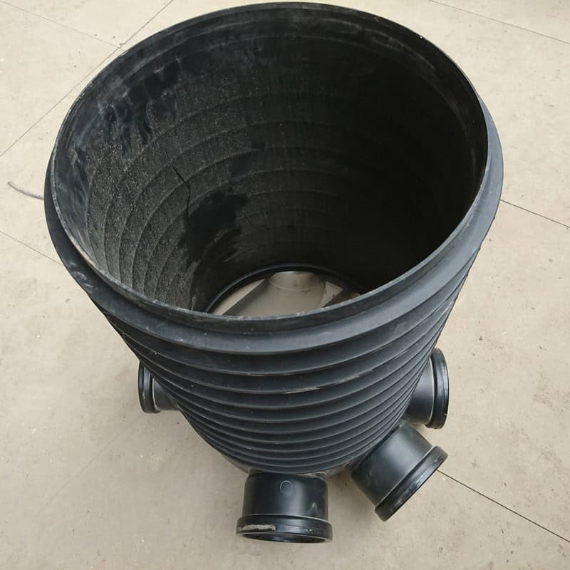 The 320mm Base & Riser, a black plastic pipe connector with a central cylinder and multiple smaller openings, stands upright on a beige tile floor.