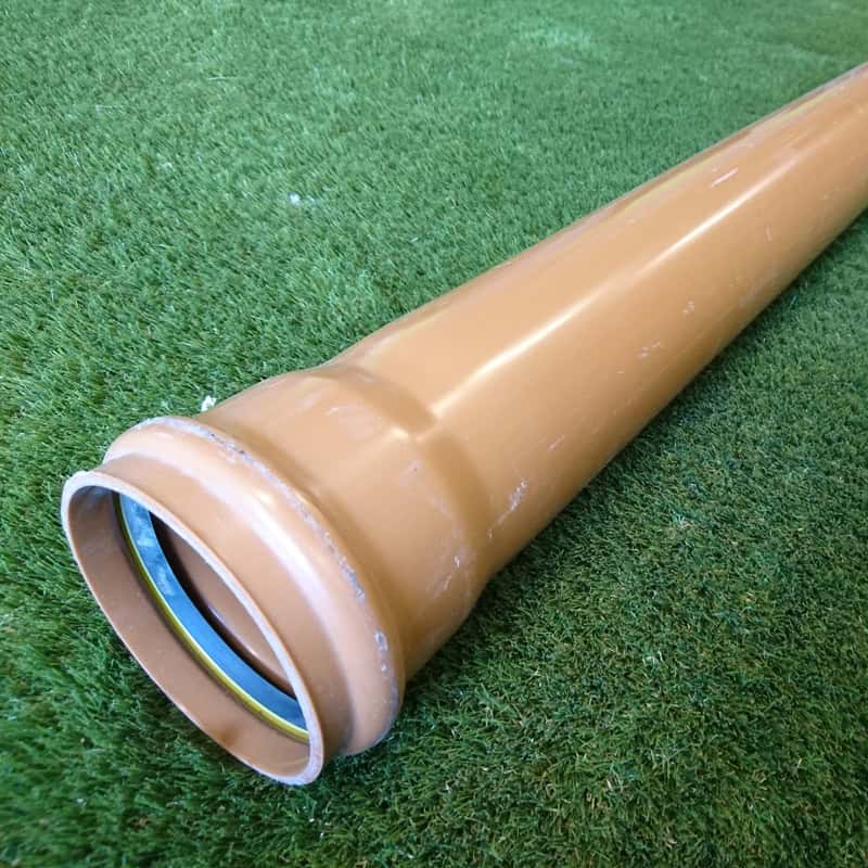 The 110mm 6mtr Single Socket Pipe with a brown PVC body is on a grassy surface, featuring a yellow and black rubber seal at the flared end for secure connections.