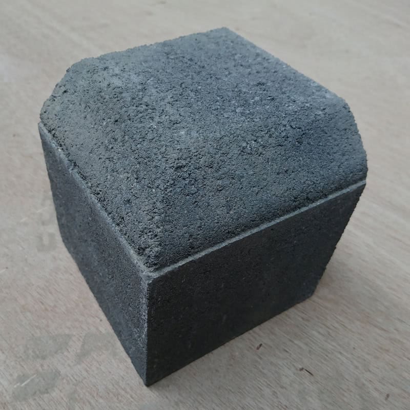 The Barleystone Paving 2 Way Small External Corner, with its textured dark gray trapezoidal concrete design, rests elegantly on a light wooden surface.