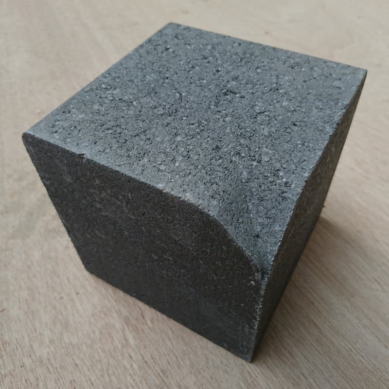 A gray textured cement cube on a wooden table resembles the Barleystone Paving 2 Way Small Internal Corner, showcasing its design with a gracefully curved indentation.