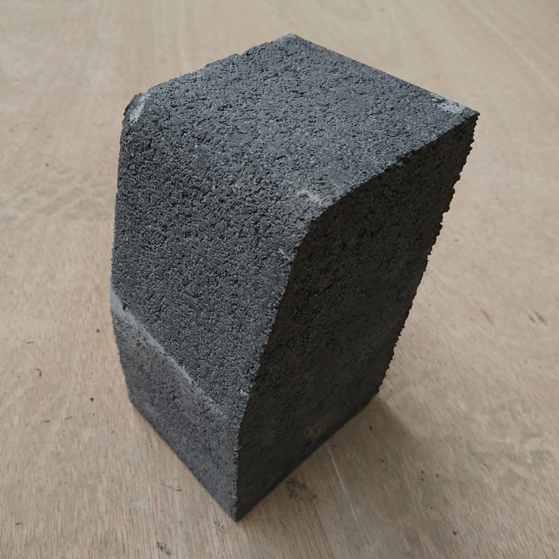 A Barleystone Paving 3 Way Large Kerb High brick in gray stands vertically on wood, showing its textured and porous surface.