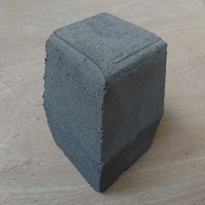 A close-up of a gray, rectangular block with a textured surface and rounded edges stands upright on wood. Its high porosity resembles Barleystone Paving 3 Way Large External Corner High, adding an uneven texture to its design and highlighting its porous material.