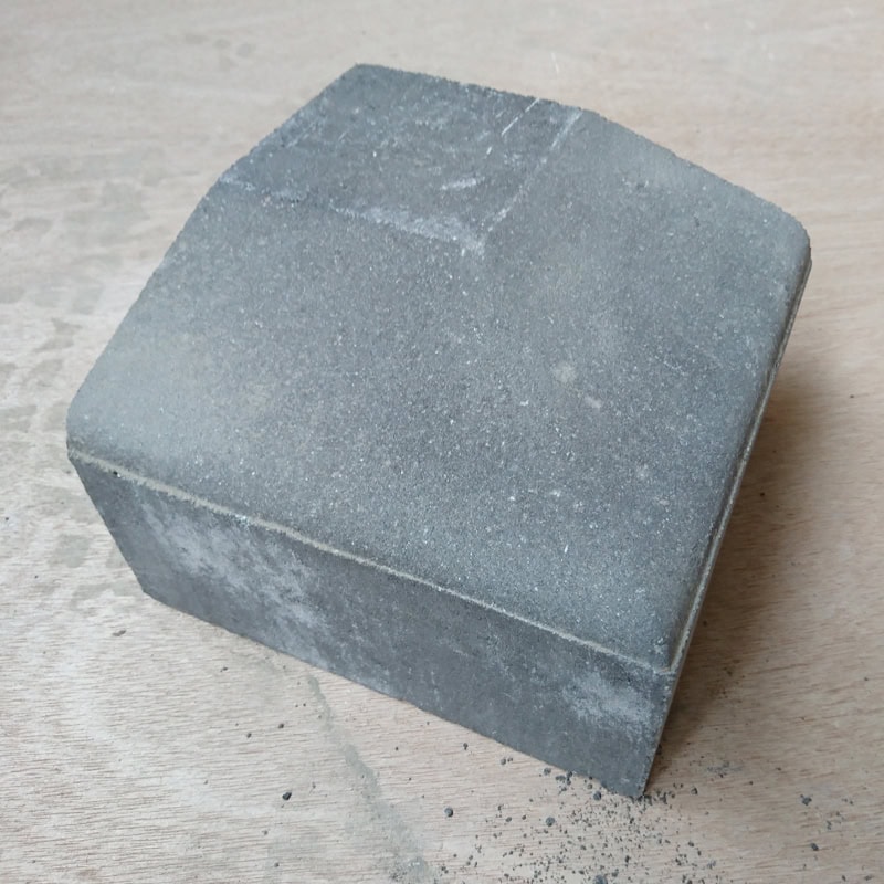 A gray Barleystone Paving 3 Way Large External Corner Low block with a sloped top rests on a wooden surface, appearing slightly dusty and worn along the edges.