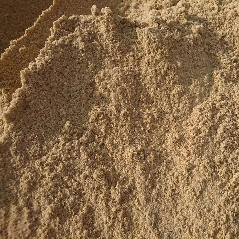 Close-up of a pile of Sharp Sand - Loose with a textured surface and subtle shadows. The grains vary in color, creating a natural, uneven appearance reminiscent of sand found on pristine beaches.