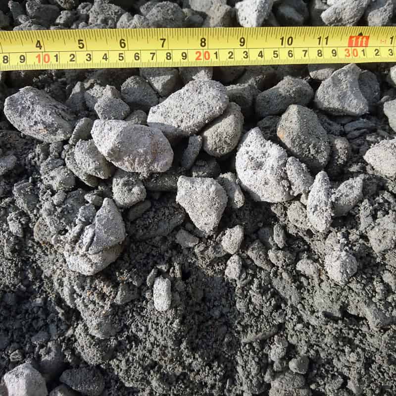 A close-up of a pile of grayish Type 1 Crushed Granite - Bagged stones, varying from small to medium sizes, with a yellow measuring tape above them. The rough textures and uneven shapes are perfect for your next project.