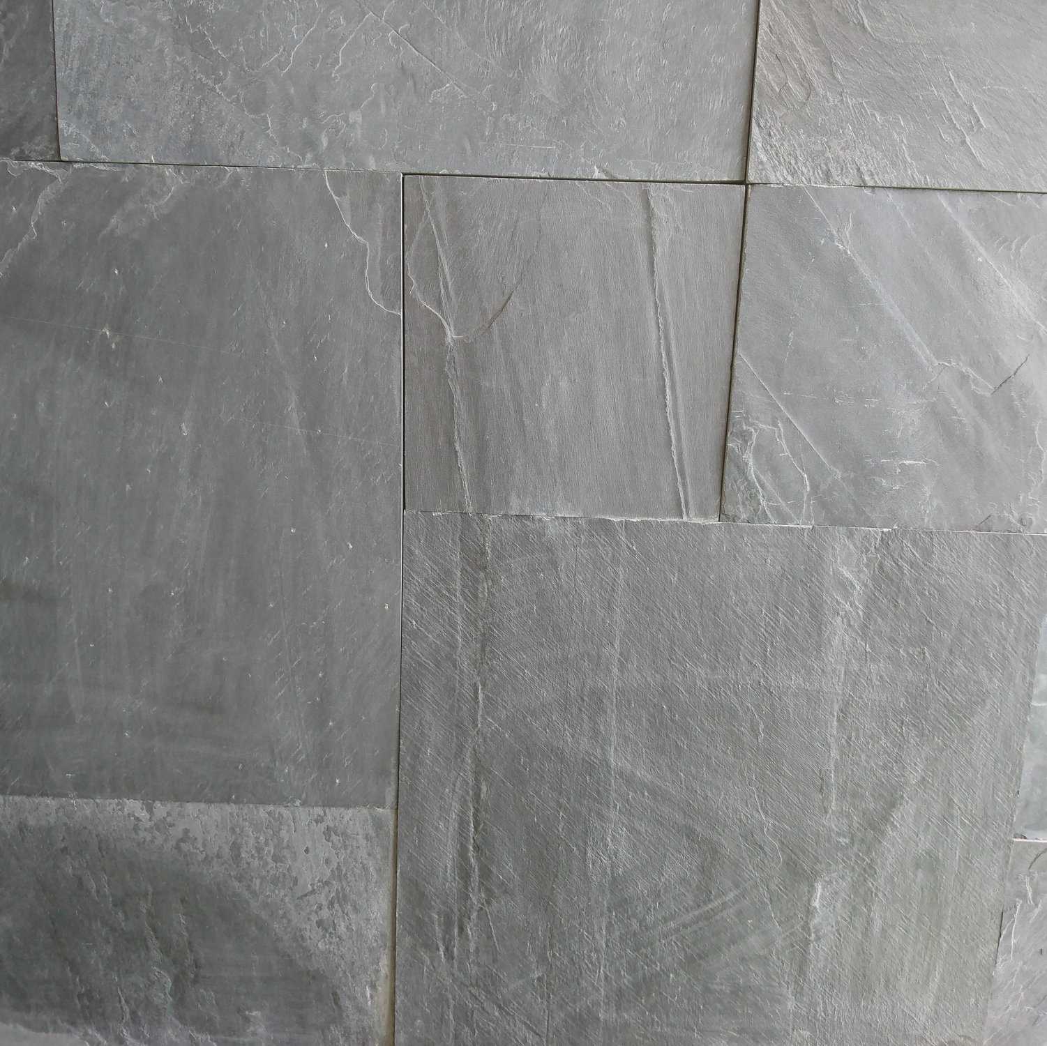 Close-up of a textured gray stone wall featuring Strata 22mm Calibrated Olive Black Slate slabs in a grid pattern. Natural variations and subtle cracks enhance the rustic appearance, adding depth and character to the surface.