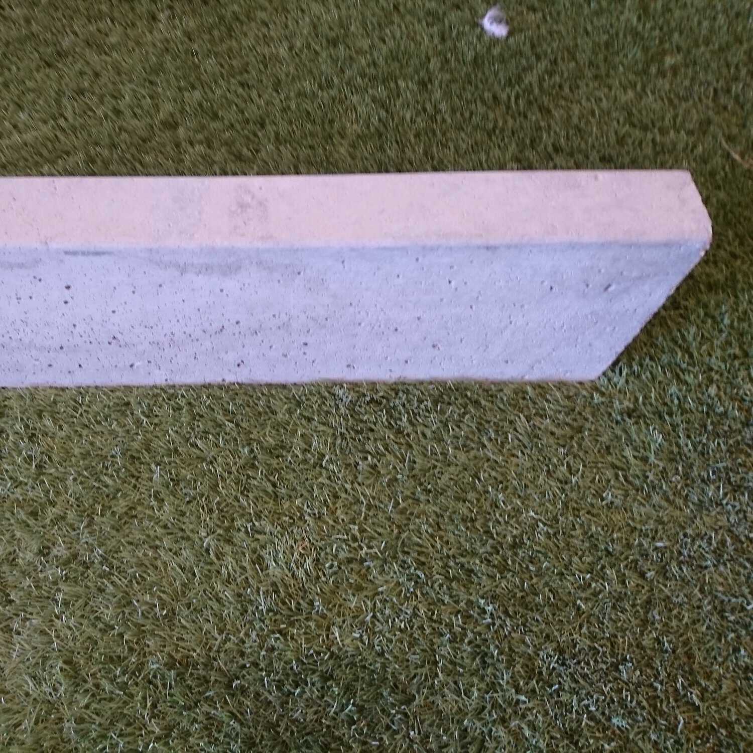 A long, rectangular Supreme Flat Top Path Edging Natural slab lies diagonally on artificial green grass, with a slightly textured surface and small speckles.