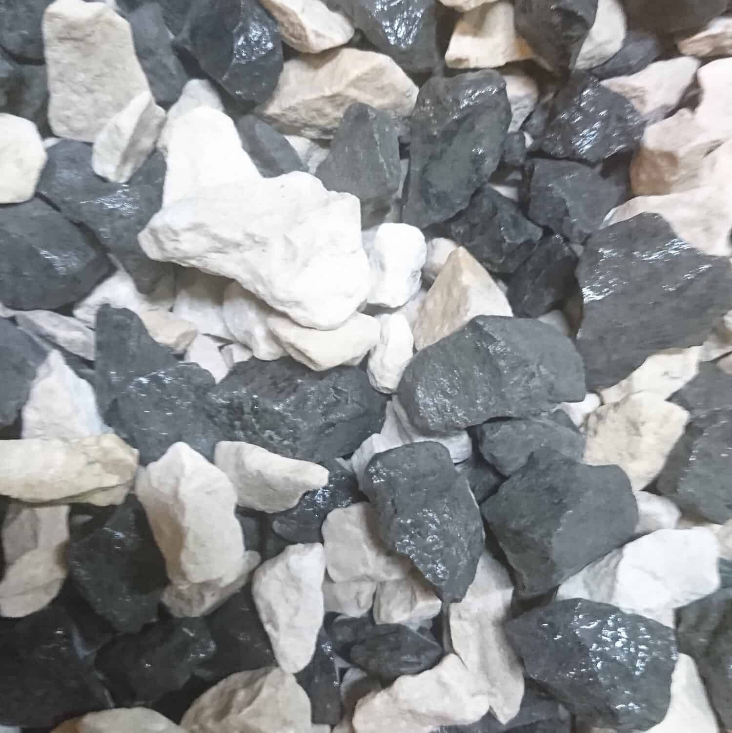 Close-up of a bagged pile of Salt & Pepper Chippings 14-20mm, showcasing a mix of dark gray and white stones with a glossy damp texture. The irregularly shaped rocks are tightly packed together.