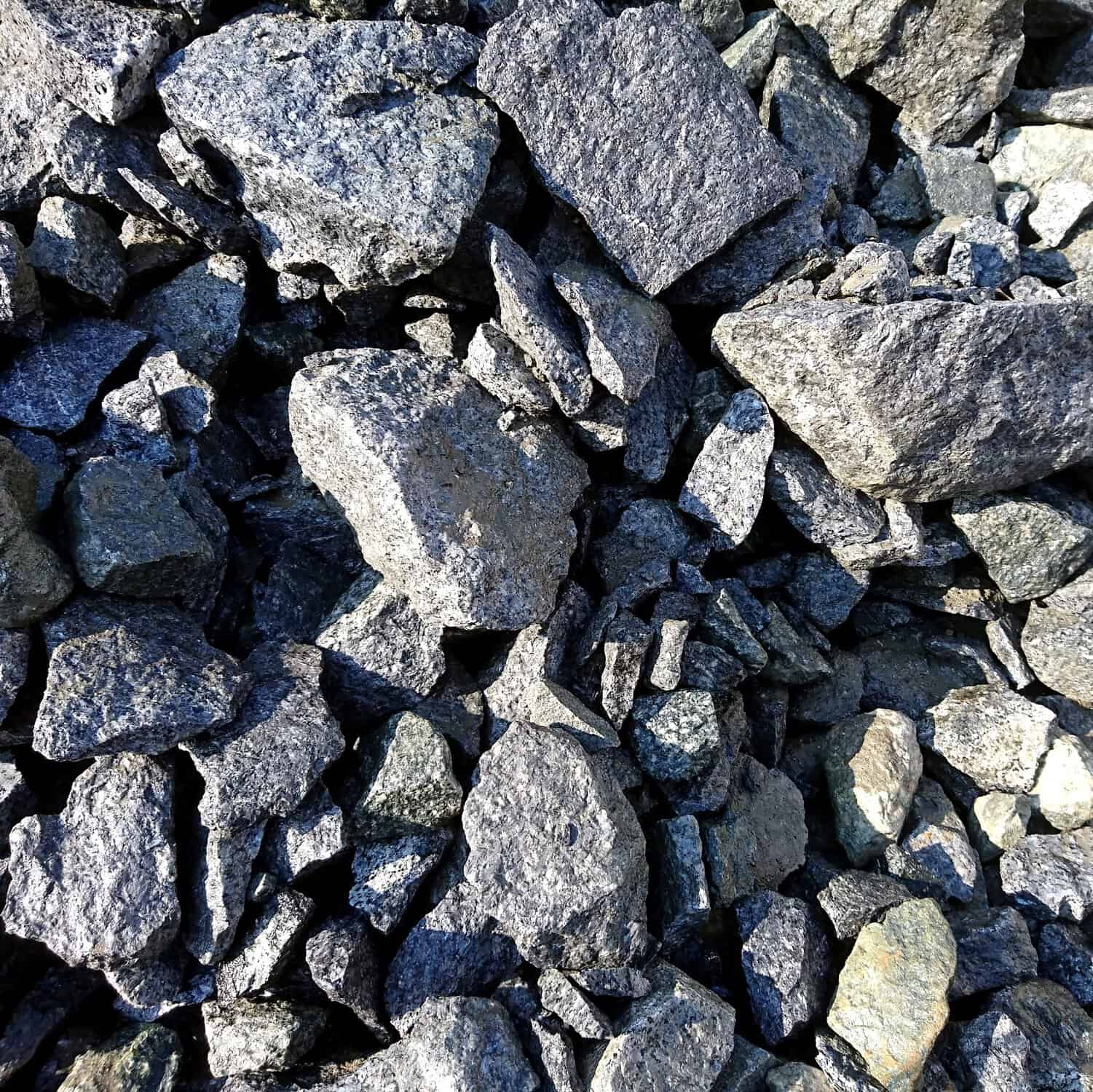 A close-up showcases Sparkling Granite Mixed Size Rocks, packed tightly together. Their jagged, irregular shapes and rough texture catch the sunlight, creating a slightly sparkling appearance.