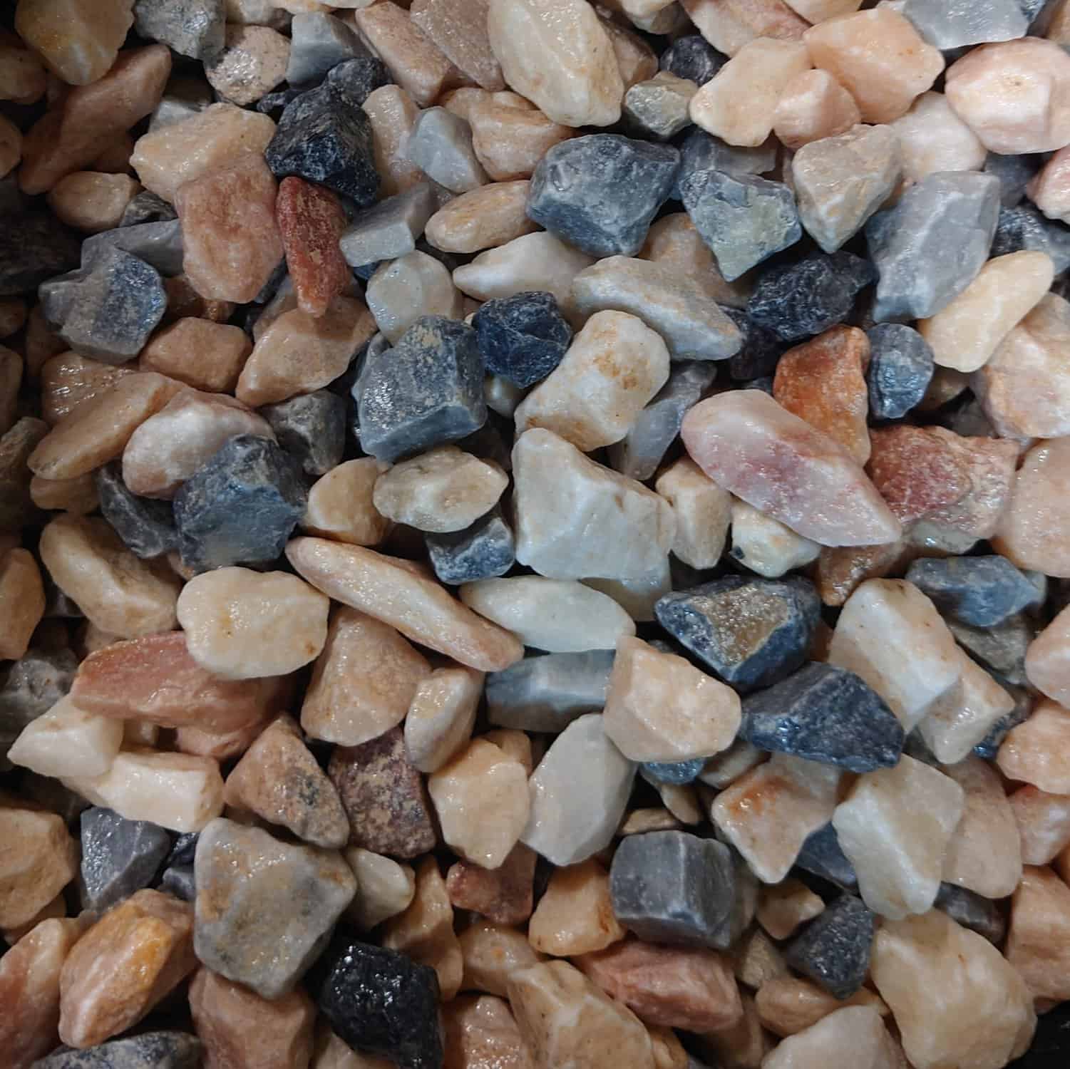 A close-up of Flamingo Chippings 14-20mm - Loose, featuring assorted small stones in beige, gray, white, and brown. These unevenly shaped rocks are loosely packed for a textured appearance.