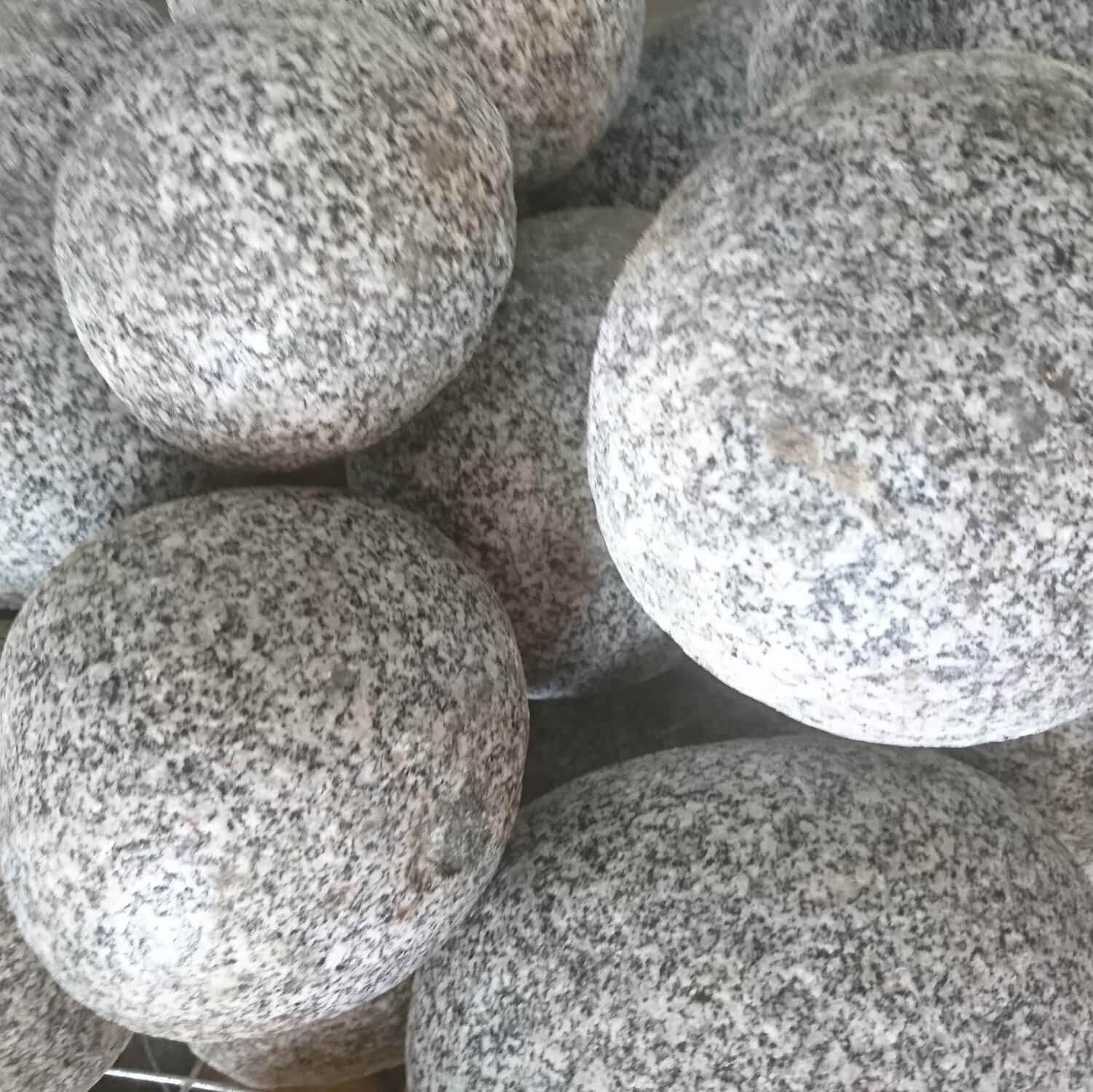 Close-up of 200-300 Silver Grey Rounded Boulders with a speckled gray and white texture. The smooth, similarly-sized boulders are tightly stacked together.