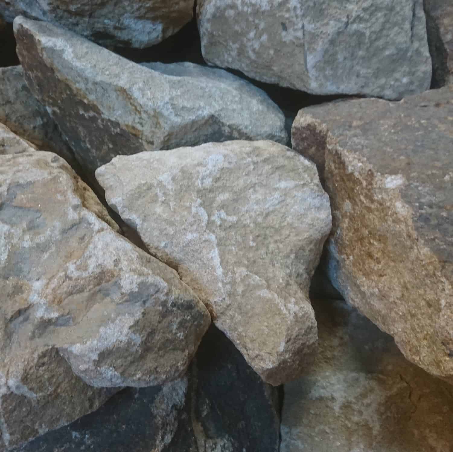 A close-up view showcases a rugged pile of 300-400mm Yorkstone Rockery stones, irregularly shaped with shades of gray and brown, featuring textured surfaces and natural fractures for an authentic look.