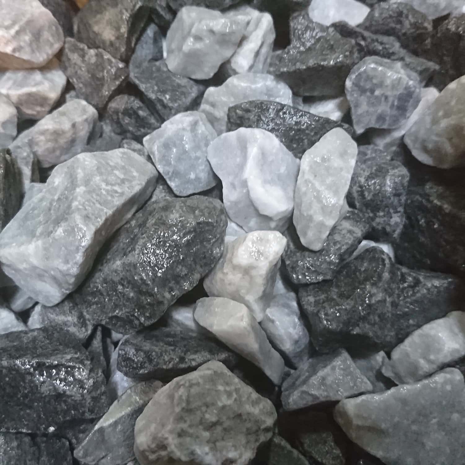 A loose assortment of rocks including Black Ice Chippings 14-20mm, consisting of mixed dark and light gray stones with varied sizes and rough textures.