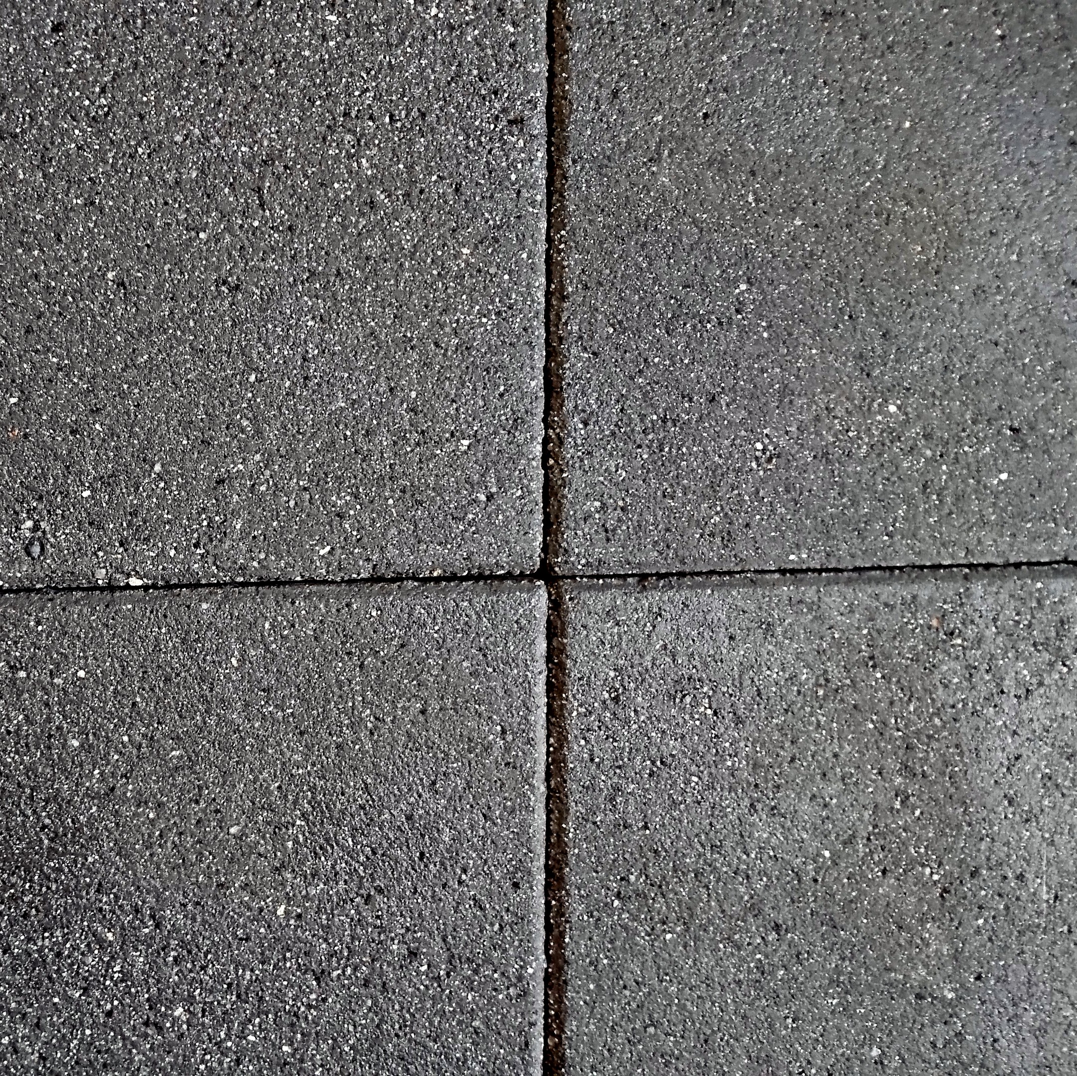 Close-up of a textured dark gray pavement showcases Barleystone Granite Paving Slabs Black in a grid pattern, with a slightly rough surface and visible spaces forming a cross at the center.