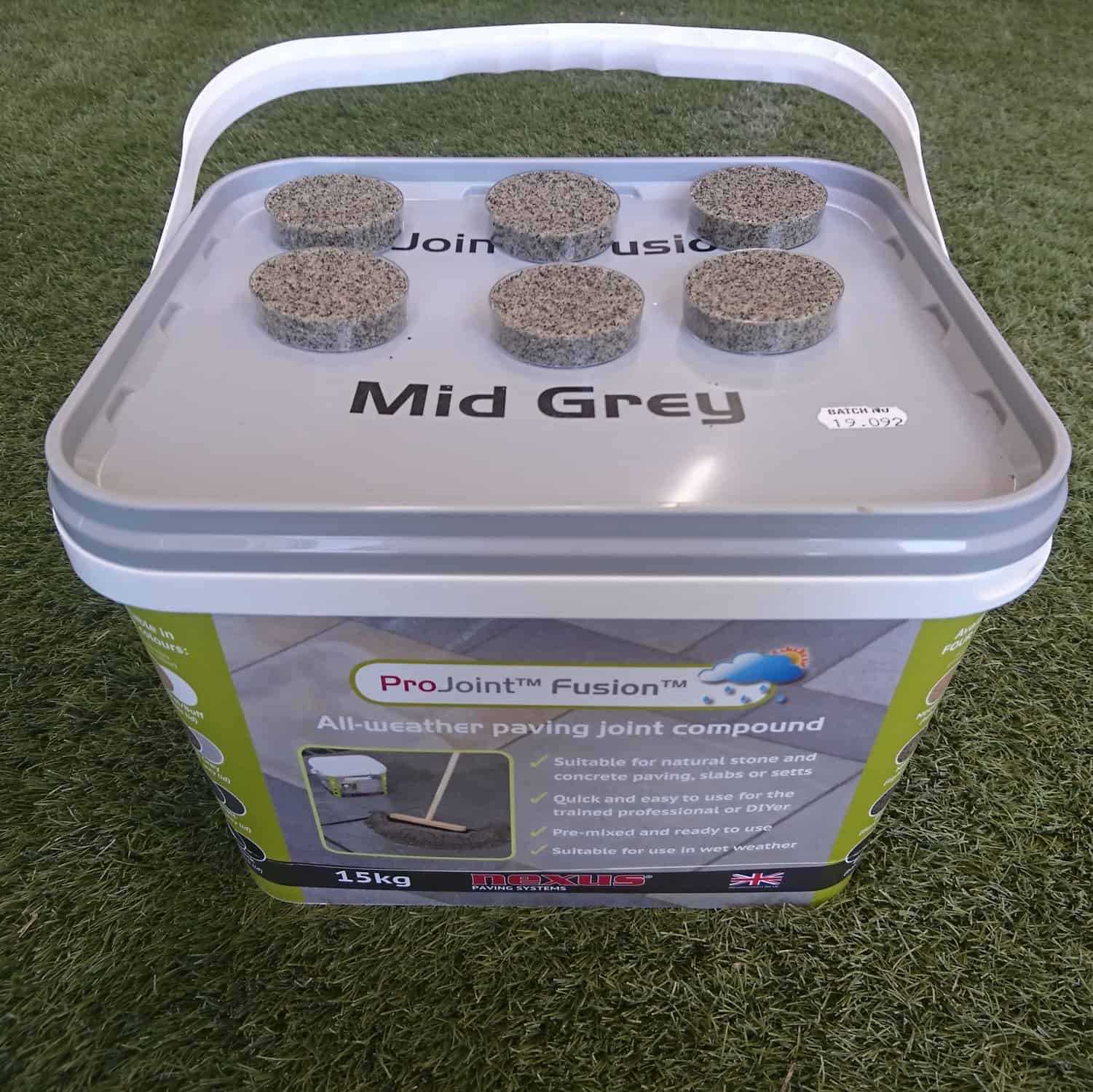 A 15kg ProJoint Fusion Mid Grey Paving Joint Compound bucket for natural stone and concrete paving rests on grass. Its lid displays six circular samples, labeled as the ultimate Paving Joint Compound, and is priced at £39.99.