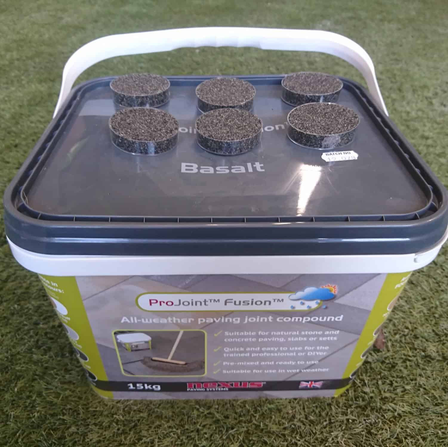 A 15 kg container of ProJoint Fusion Basalt Paving Joint Compound sits on grass with its front label and six foam pads on the lid showing, ideal for efficient paving tasks.