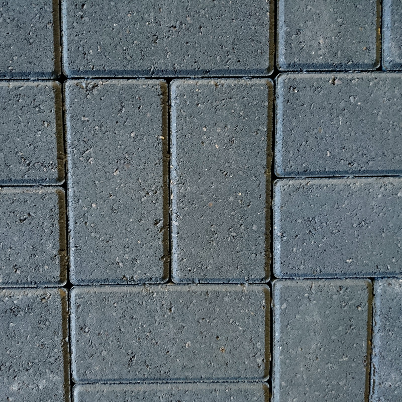 Close-up of a pavement with rectangular tiles in a grid pattern. The Breedon 50mm Drive Charcoal tiles are uniformly gray, slightly rough-textured, with thin gaps showing subtle charcoal tones typical of Breedon surfaces.