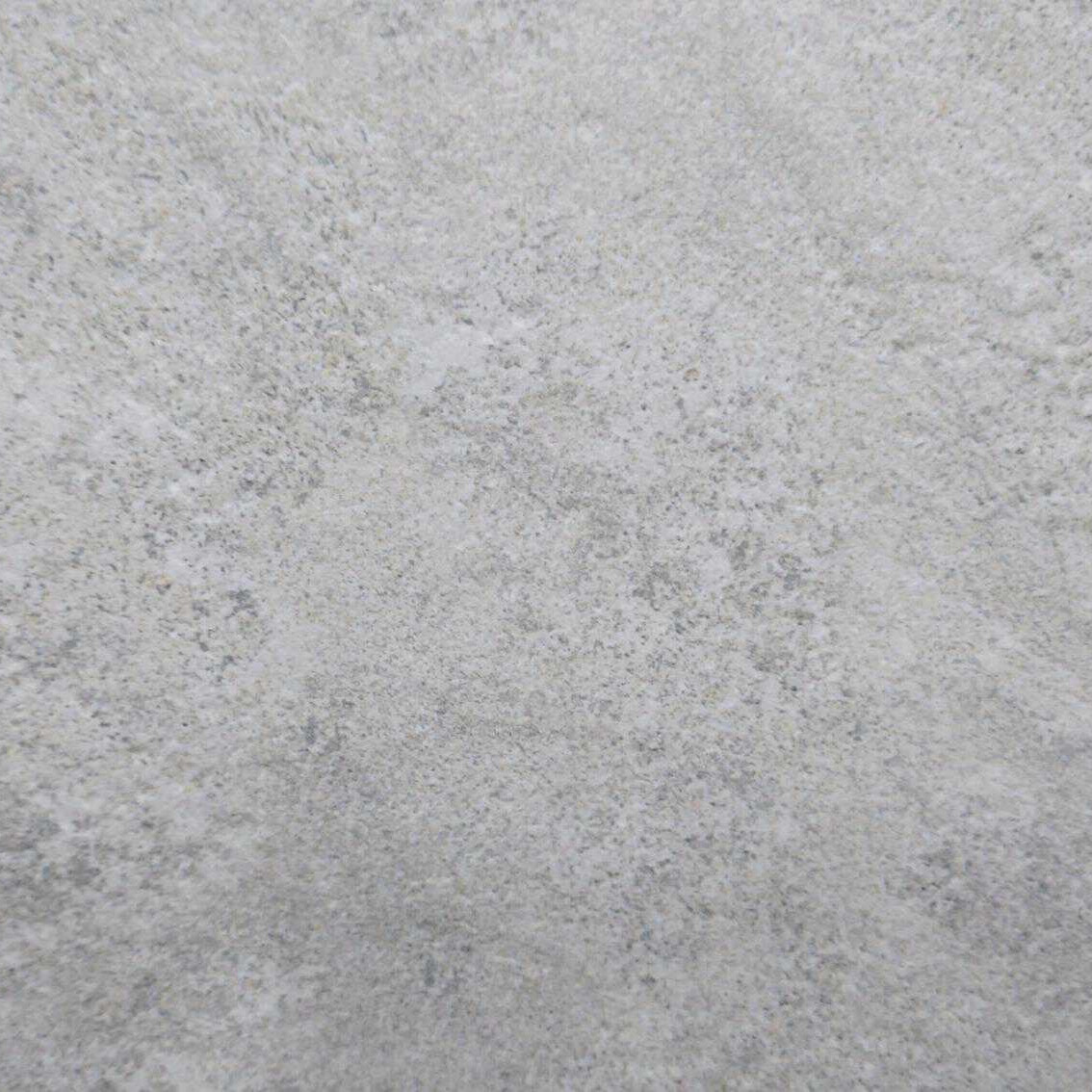 A close-up view of Premier Himalayan White Porcelain 900x600x20mm reveals a light gray, speckled surface with grainy, stone-like texture and natural uneven patterns. Subtle color variations in white and dark gray are dispersed throughout the 900x600 format at 20mm thickness.