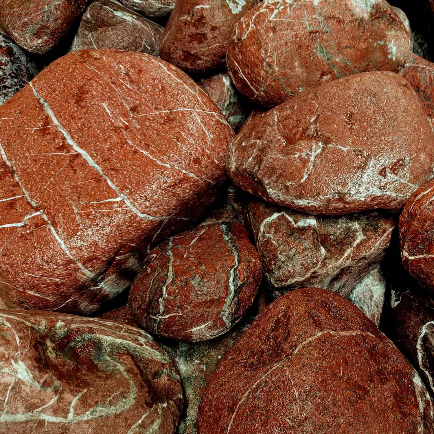 The 100-200 Red Laguna Boulders feature reddish-brown hues, white veins, and rough surfaces, creating a tightly packed textured and natural pattern.