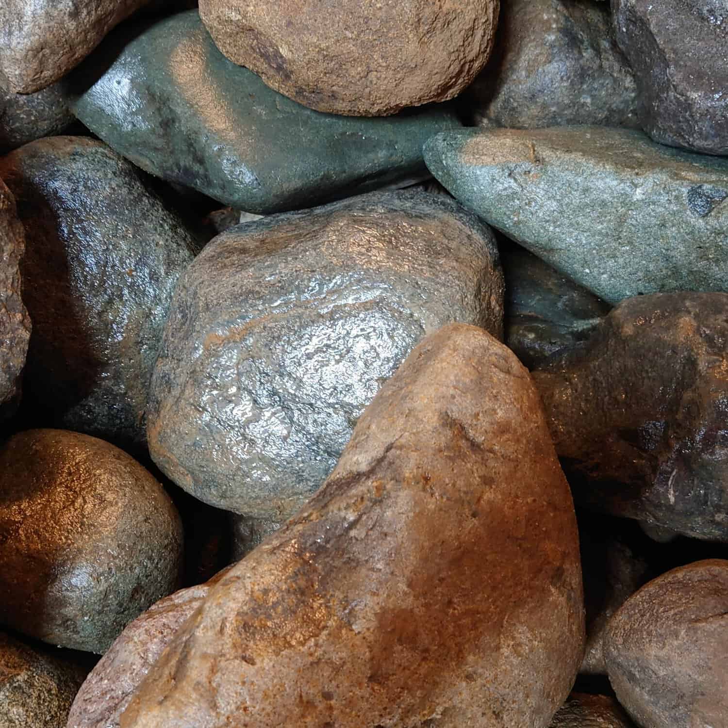 Close-up of 200-300mm Cambrian Cobbles, showcasing smooth, variously shaped river rocks in shades of brown, gray, and green. They feature subtle textures and a slightly glossy finish that captures their natural essence.