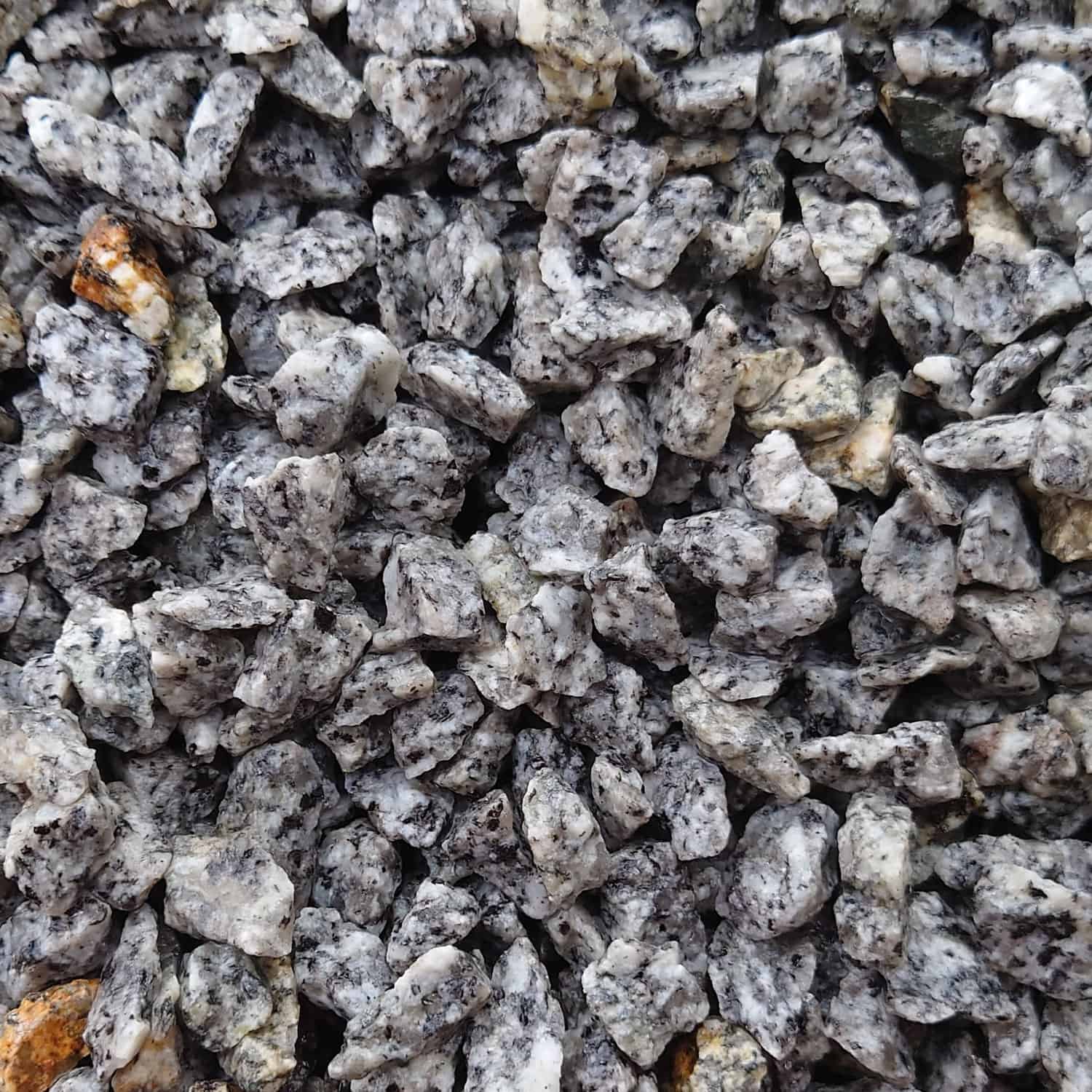 A close-up of Silver Quarts Granite 14mm-Loose gravel reveals a speckled gray, black, and white pattern with occasional brown hints, adding contrast to the cool-toned composition.